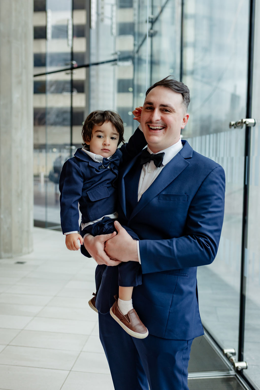 Groom holding a young ring bearer in matching navy suits